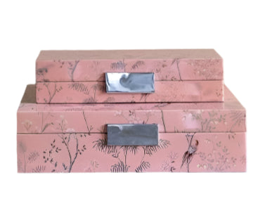 The Addison Ross Pink Chinoiserie Box Collection features two stacked pink rectangular boxes with floral patterns and metallic handles that provide elegant jewelry storage, embodying the charm of the brand Addison Ross.