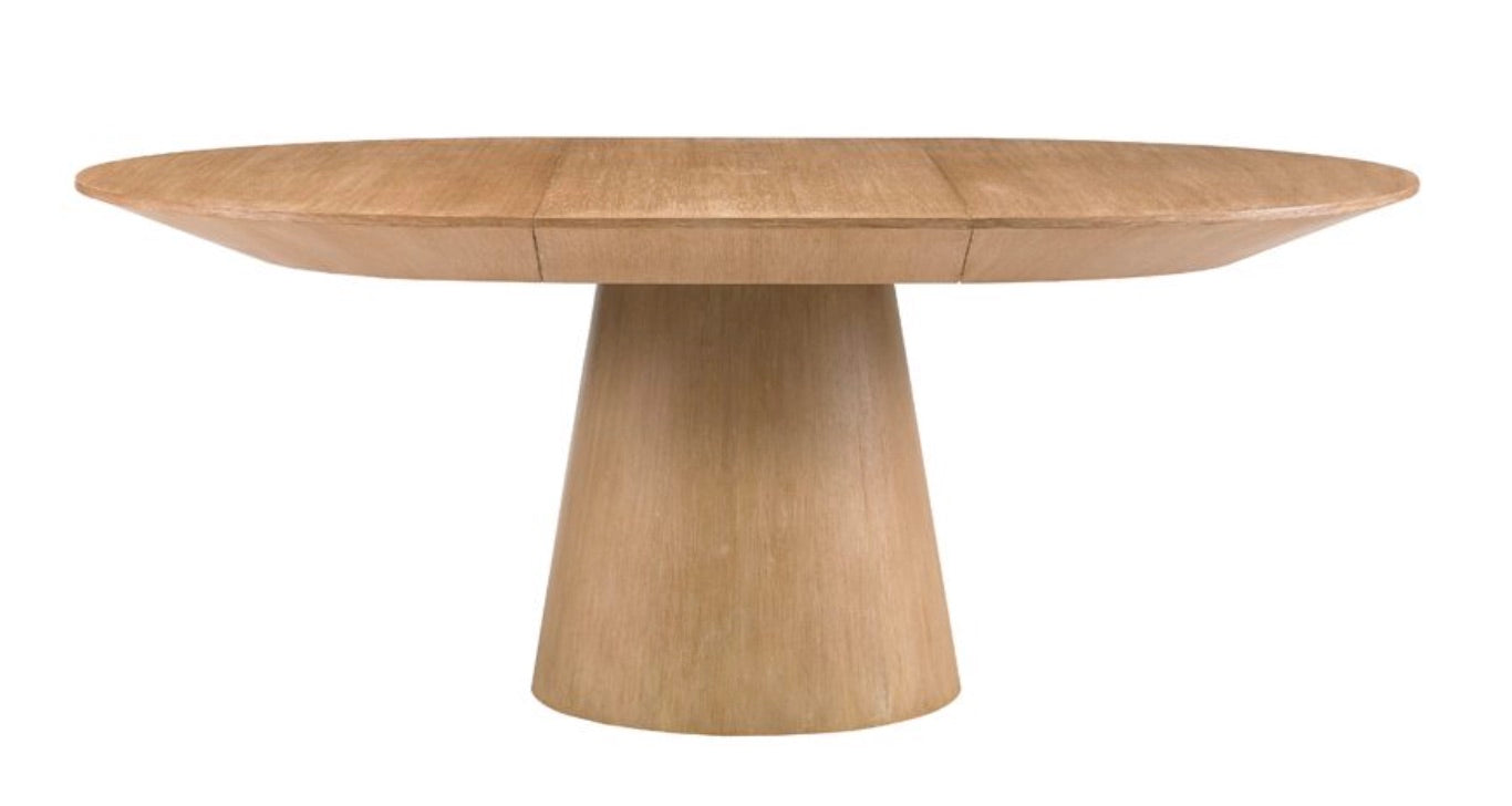 The Discus Extendable Dining Table by Sherrill/Mr & Mrs Howard features an oval top and wide conical pedestal base, crafted from natural oak and presented against a white background.