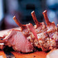 Sliced rack of cooked lamb with exposed bones, inspired by the cookbook Barefoot in Paris from Penguin Random House, resting on a wooden cutting board.