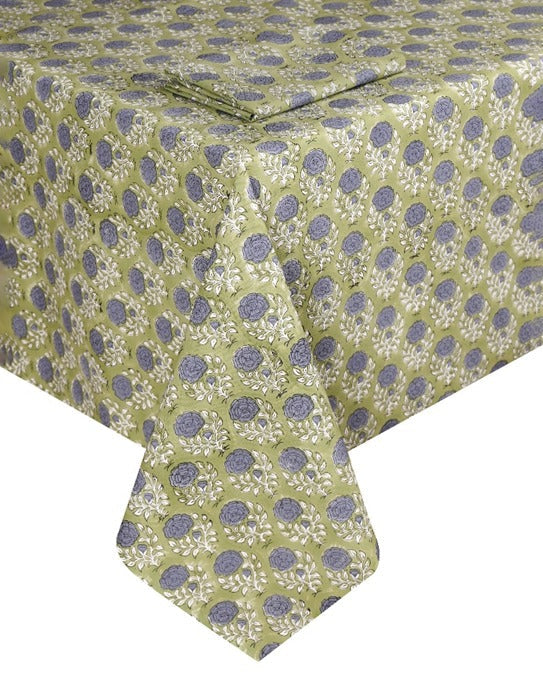 A rectangular table is set with artisanal tableware and the Lily Table Linen Collection by SLOANE BY HAND, featuring a green fabric with a repeating blue and white floral design.