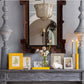 A mantelpiece with candles, framed photos, a mirror, and a vase with flowers features the Addison Ross Chinoiserie Frame Collection. A chandelier and wall sconce are visible in the mirror's reflection.