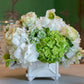 The Hive Floral Studio Live Classic Floral Arrangement features white and green sympathy flowers in a small, elegant ceramic vase, perfect for display on a table.