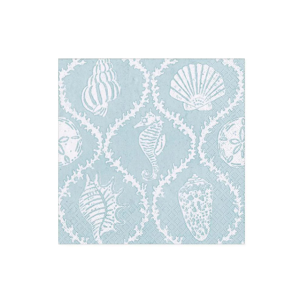 The Seychelles Aqua Collection napkin by Caspari features a light blue square triple-ply design with white outlines of seashells, sand dollars, and a seahorse in a repeating pattern.