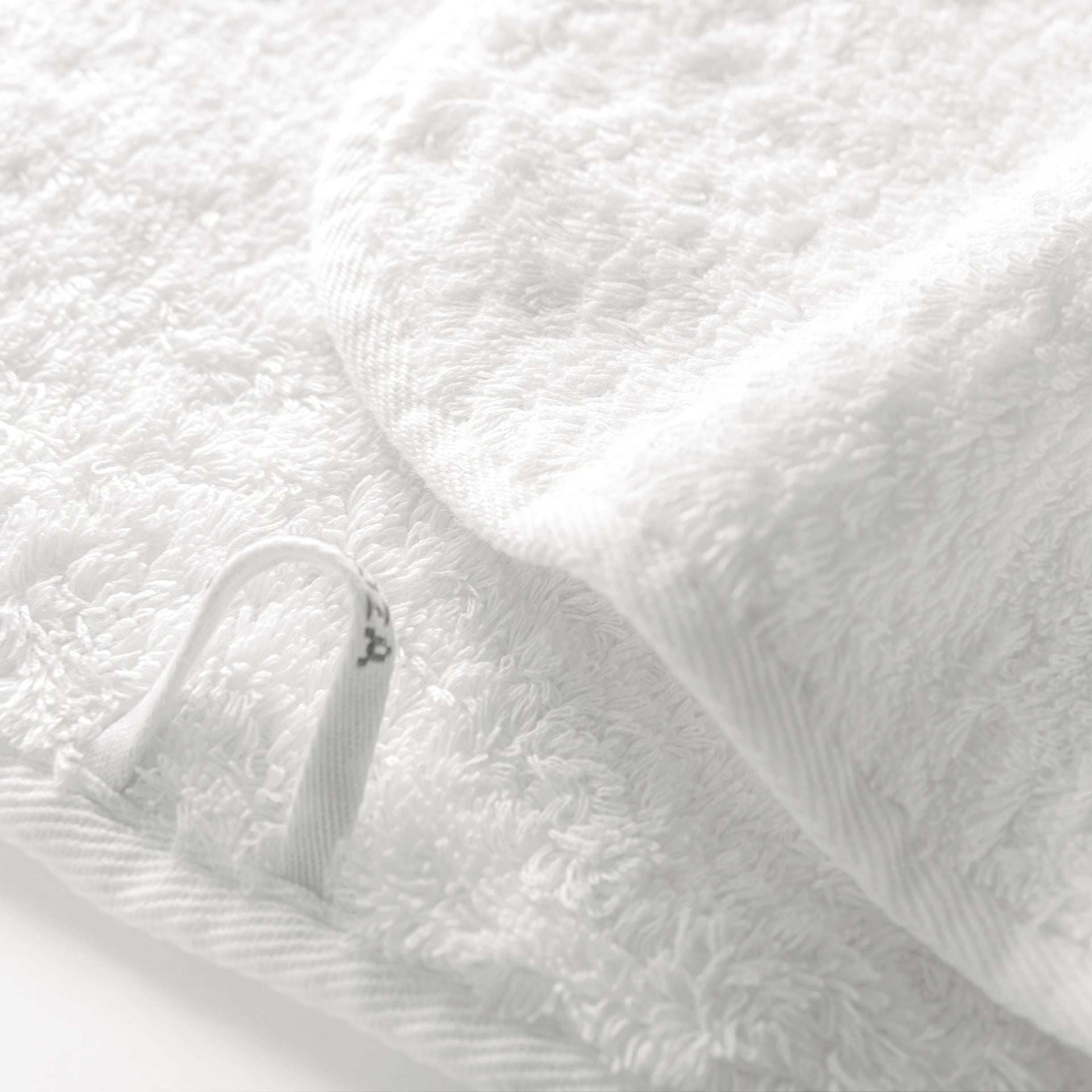 Close-up of a folded white towel from the Graccioza Egoist Bath Collection, made of Egyptian cotton terry cloth, featuring a small fabric hanging loop.