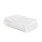 A folded white towel from the GRACCIOZA Bee Waffle Bath Collection, featuring a soft honeycomb texture, rests on a white surface.