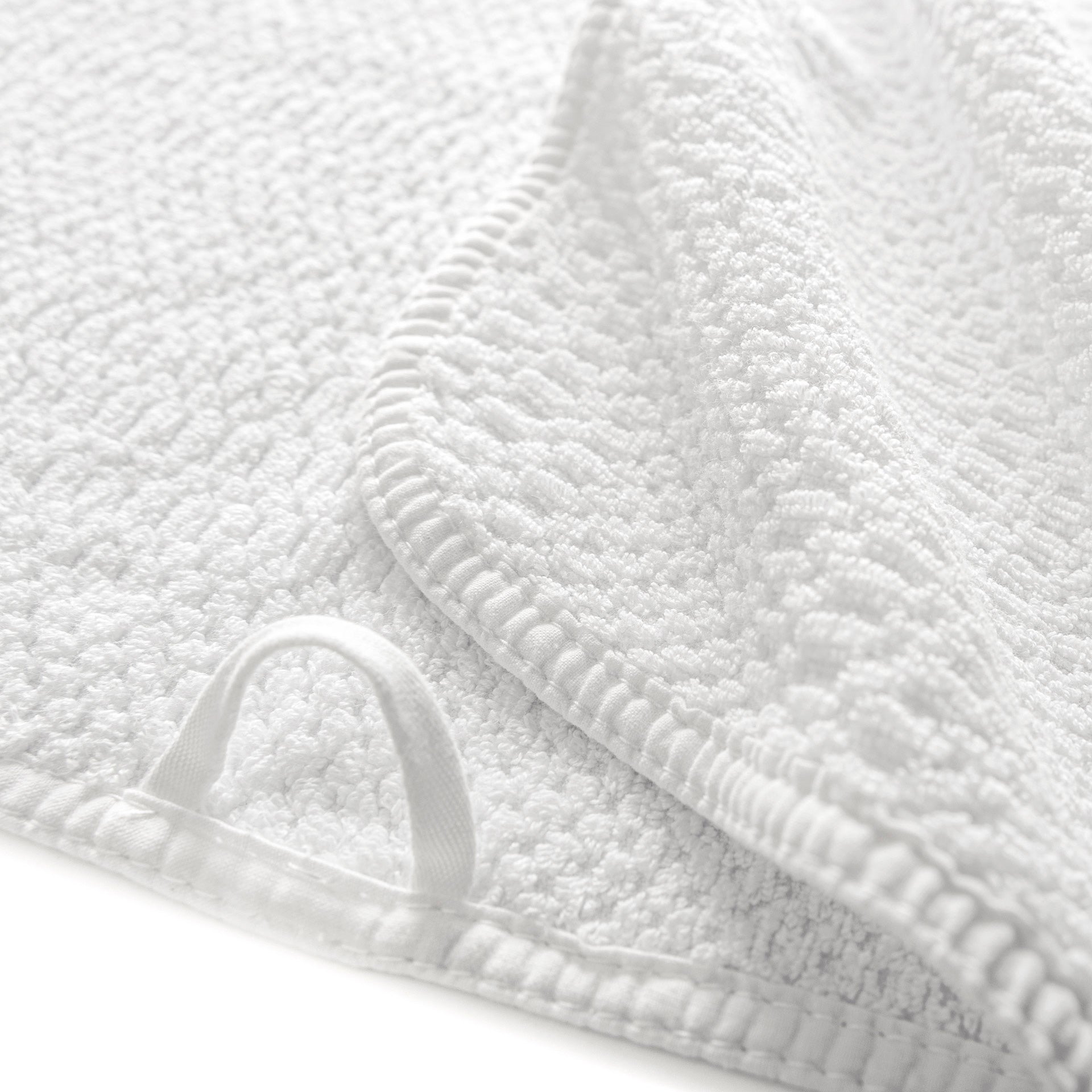 Close-up of the GRACCIOZA Bee Waffle Bath Collection: a white combed cotton towel featuring stitched edges, honeycomb texture, and a fabric hanging loop.