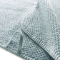 Close-up of the Bee Waffle Bath Collection towel by GRACCIOZA, featuring a textured light blue honeycomb weave with a folded corner and looped tag, crafted from premium combed cotton.