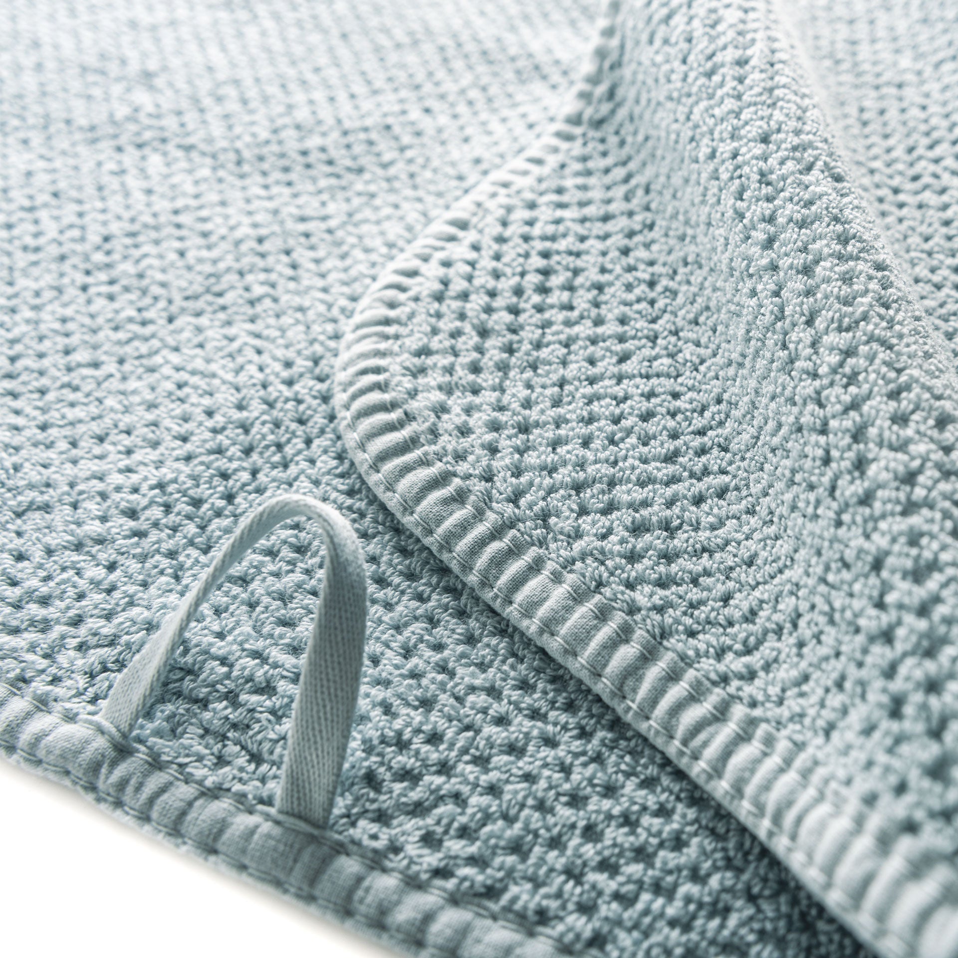 Close-up of the Bee Waffle Bath Collection towel by GRACCIOZA, featuring a textured light blue honeycomb weave with a folded corner and looped tag, crafted from premium combed cotton.