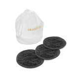 Three round black Egoist Spa Accessories makeup remover pads by Graccioza, crafted from luxurious Egyptian Cotton Giza, are displayed before a white "GRACCIOZA" drawstring bag. Ideal for gentle cleansing and pairing with your favorite hair towel.
