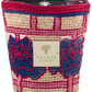A colorful Baobab Collection Frida Draozy Frida scented candle with a woven basket design in beige, blue, and pink, featuring a metallic logo plate on the front.