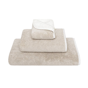 Three beige Bicolore Bath Collection towels by Gracciozza, each a different size, are stacked neatly against a white background.