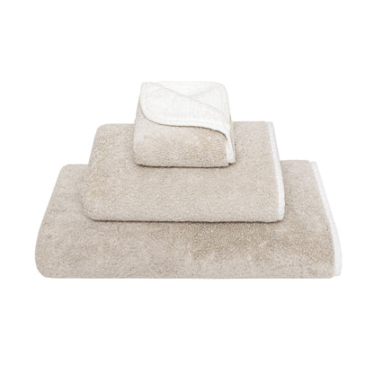 Three beige Bicolore Bath Collection towels by Gracciozza, each a different size, are stacked neatly against a white background.
