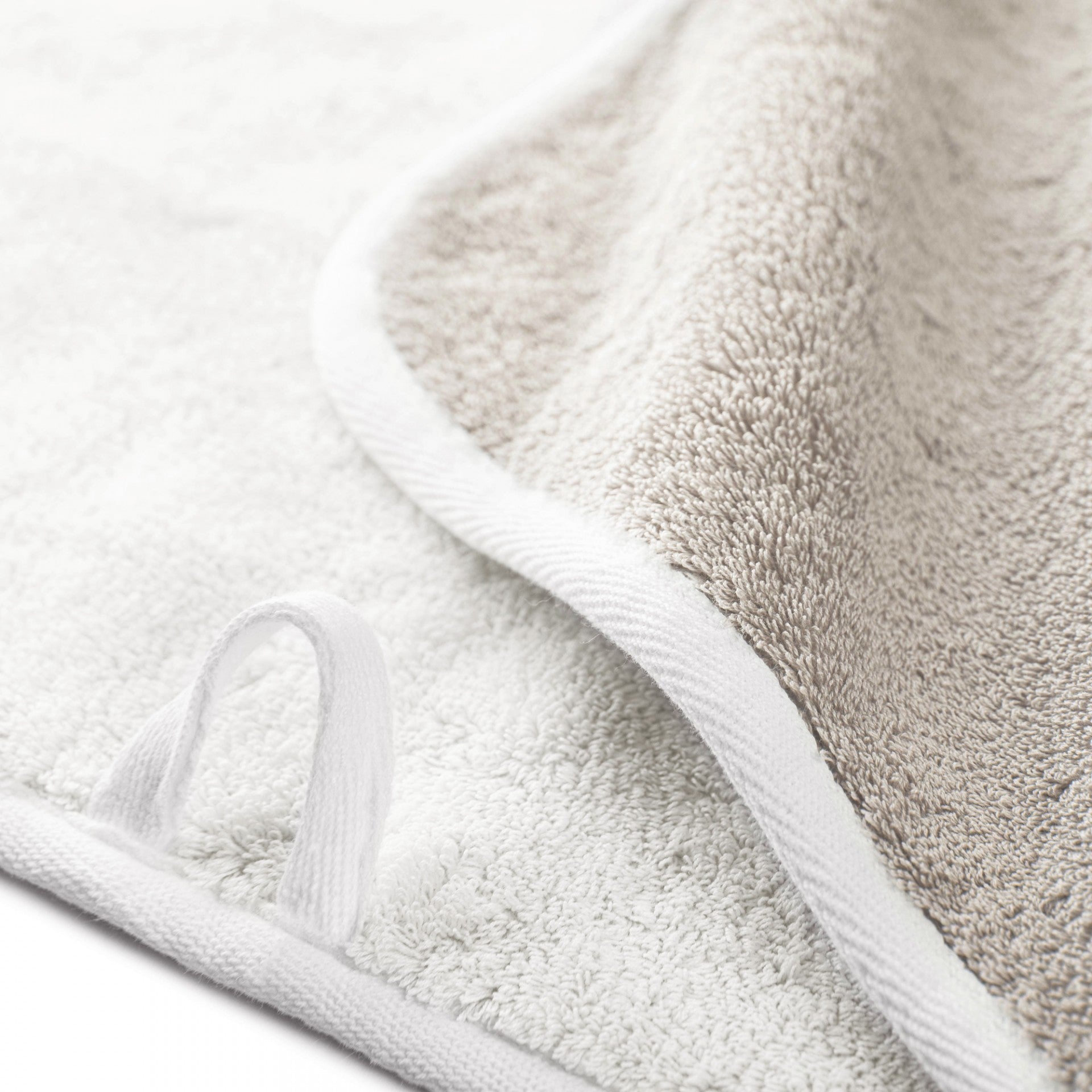 Close-up of a white and beige Graciozza Bicolore Bath Collection towel featuring a fabric hanging loop, showcasing the double-sided Egyptian cotton texture and finished edges.