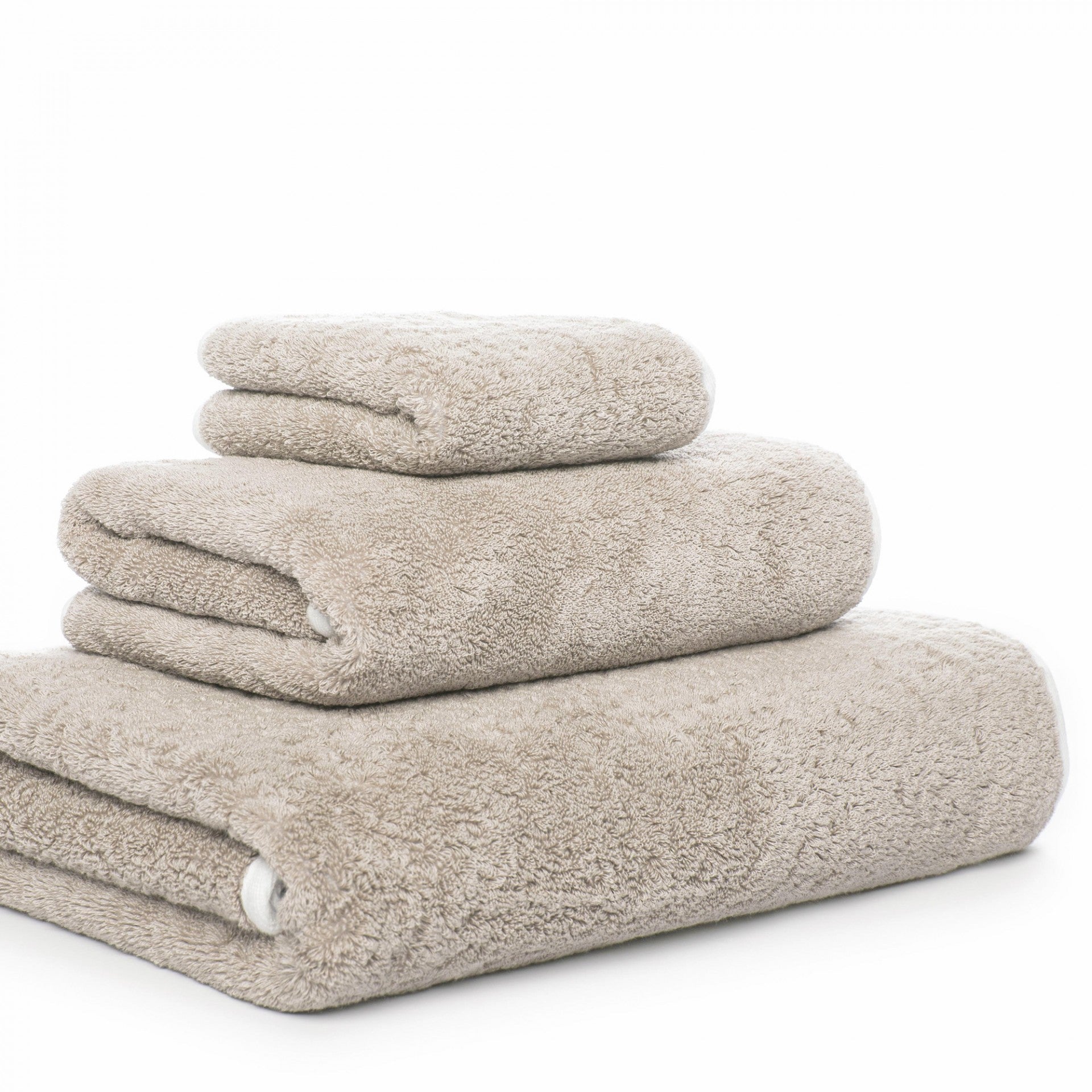 Three beige towels from the Graciozza Bicolore Bath Collection, each a different size, are neatly stacked against a white background.
