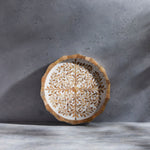 The Mya Inlay Serving and Decor Collection by Be Home features a round decorative plate with a beige and brown leaf pattern on a light gray textured surface, perfect as an elegant floral serving tray.