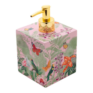 The Caspari Paradise Garden Bath Collection features a square soap dispenser with a gold pump, adorned with tropical floral and bird designs on pink, handcrafted in Vietnam using lacquerware techniques.