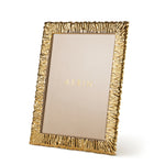 A gold-tone frame from the Ambroise Frame Collection by Aerin features a textured, wavy brass-plated border and stands upright with "AERIN" shown on a beige insert.
