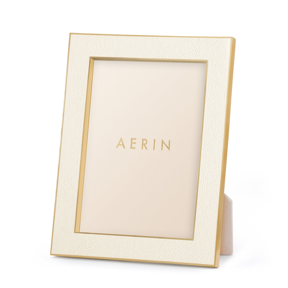 The Cream Classic Shagreen Frame Collection by Aerin features a gold-accented, embossed cream frame with a textured finish and "AERIN" on the insert—a luxurious way to display your treasured photos.