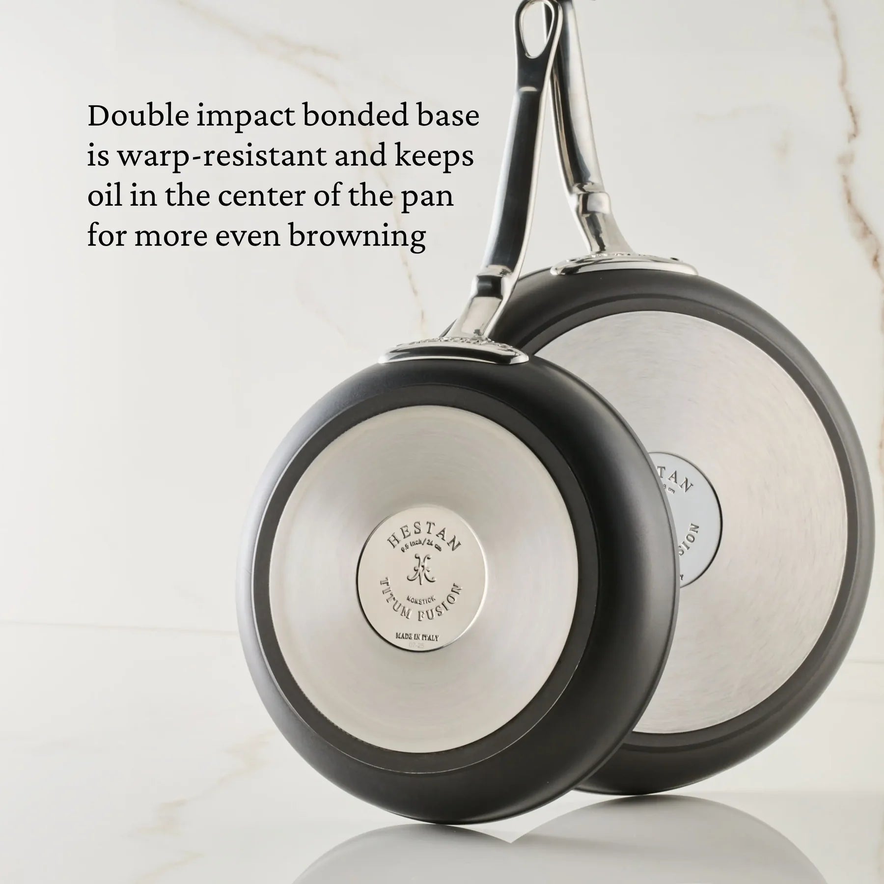 Two stainless steel frying pans from the Hestan TITUM® Fusion Collection are shown bottom side up, highlighting their brand name and diamond-reinforced cookware bases.