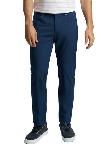 A man wearing Peter Millar Crown Comfort Five-Pocket Pant in classic fit blue trousers and black sneakers.