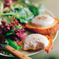 A plate featuring a mixed green salad and two perfectly poached eggs atop toasted bread, inspired by classic Parisian recipes from Penguin Random House’s Barefoot in Paris. A fork rests beside the plate.