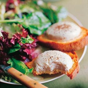A plate featuring a mixed green salad and two perfectly poached eggs atop toasted bread, inspired by classic Parisian recipes from Penguin Random House’s Barefoot in Paris. A fork rests beside the plate.