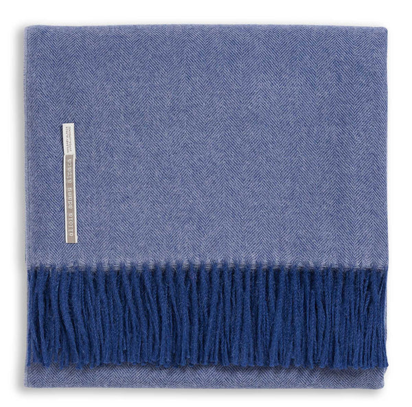 The Alicia Adams Alpaca Classic Throw in Indigo Herringbone features a luxurious baby alpaca weave with a herringbone pattern and fringe on one edge, fair-trade crafted for elegance.