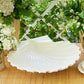 The Cream Shell Platter Collection by Aerin features a glossy white earthenware serving platter, showcased on a woven surface with baskets and white flowers—an ideal accent for coastal-inspired decor.