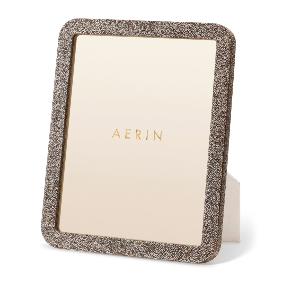 The Modern Shagreen Frame by Aerin is a rectangular standing picture frame featuring a textured brown border and minimalist design, with "AERIN" in gold letters on the insert.