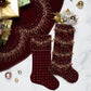 Two Kim Seybert Celestial Stockings in burgundy velvet with bead and sequin embellishments are shown on a marble surface alongside ornaments, wrapped gifts, and a coordinating tree skirt—an elegant holiday display.