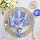 A fresh spring table set with a white plate, blue embroidered napkin, silverware, clear and blue glasses, and a floral arrangement on the Kim Seybert Herringbone Placemat—perfect for seasonal dining.
