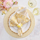 A table setting features a white plate on a yellow placemat, Kim Seybert's Provence Napkin Set with a fun pattern and napkin ring, two yellow glasses, and pink and white flowers on a matching tablecloth.