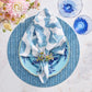 A blue and white table setting features a patterned napkin, floral napkin ring, blue plates, Kim Seybert Herringbone Placemat, blue glassware, and a floral bouquet on marble—perfect for spring and summer dining.