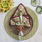 A dinner plate sits on the Kim Seybert Chevron Moss Placemat, accented by a folded napkin with ring, two green glasses, and yellow flowers in a vase atop a white table.