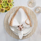 Table setting with a white plate, white napkin with tan trim held by the Kim Seybert Seashell Burst Napkin Ring, round woven placemat, two sparkling drinks, and a vase of yellow flowers—ideal for seaside gatherings.