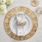 A formal place setting features a gold-rimmed plate, a white napkin with metallic beads in a Kim Seybert Fun Burst Napkin Ring, on a textured charger, accented by flowers and two glasses.