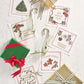 Two wrapped gifts, two champagne flutes with candy canes, and a Kim Seybert Merry and Bright Cocktail Napkin Set arranged on a white wooden surface—an ideal choice for a cheerful hostess gift.