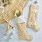 Two gold and white stockings from the Kim Seybert Gilded Sparkle Stocking and Tree Skirt Collection, adorned with sequins and beads, rest on marble alongside metallic ornaments, a wrapped gift, decor accents, and the matching tree skirt.