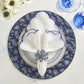 A table setting featuring the Kim Seybert Lune Napkin Set with scalloped edges, a blue and white patterned plate, a blue floral napkin ring, two blue glasses, and white flowers on the side.