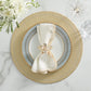 A place setting featuring the Kim Seybert Starry Night Placemat Collection, a patterned plate, white napkin with a decorative ring, and a glass of water on a white marble surface with white flowers in the upper left.