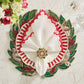 A festive table setting features a leaf charger, red and white napkins with Kim Seybert’s Gem Wreath Napkin Ring Set, two wine glasses, and fresh flowers decorating the corner.