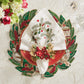 A festive holiday table set with a red plate, embroidered linen napkin, beaded leaf placemat, floral napkin ring, and glassware atop the Kim Seybert Christmas Carol Table Linen Collection.