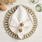 A white napkin in a Kim Seybert Casbah Napkin Ring sits on a decorative plate and placemat, complemented by dried flowers, two green glasses, and organic raffia accents for an elegant table setting.
