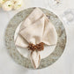 A beige napkin with a brown ring sits on a white plate and the Kim Seybert Chalet Placemat, creating nature-inspired table decor beside glasses and white flowers.