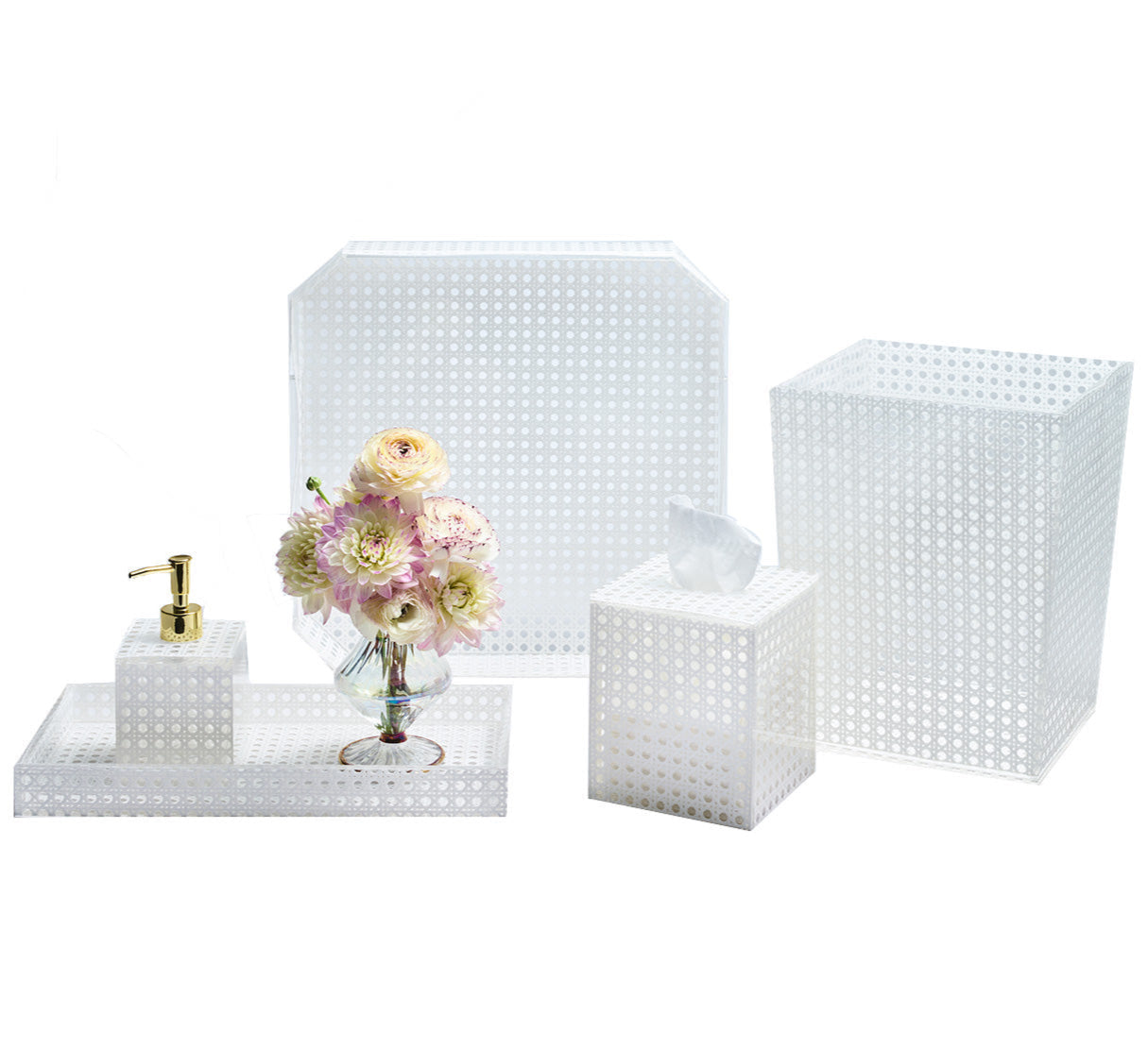 The Kim Seybert White Reed Bath Collection features white perforated accessories with a subtle reed pattern—includes a tray, soap dispenser, tissue box, waste bin, and a vase with assorted flowers.