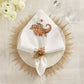 White dinner napkin with an embroidered cornucopia and pumpkins, secured by a Kim Seybert Gilded Gourd Napkin Ring on a decorative charger plate for an elegant fall tablescape.