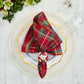 A red and green plaid napkin held by a Kim Seybert Santa Napkin Ring on a white plate with a gold rim for festive Christmas table decor.