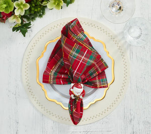 A red and green plaid napkin held by a Kim Seybert Santa Napkin Ring on a white plate with a gold rim for festive Christmas table decor.