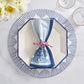The Kim Seybert Filigree Napkin Set is displayed atop a white octagonal plate with blue trim, accented by a braided cord and surrounded by flowers and glassware for an artisanal touch.