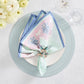 The Kim Seybert Filigree Napkin Set features a folded pastel cotton napkin and decorative filigree ring on a white plate with light blue placemat, glass, and white flowers—showcasing exquisite artisanal craftsmanship.